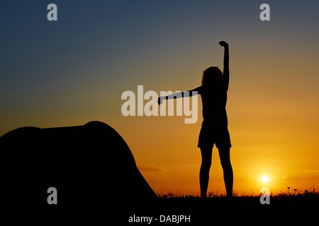 Silhouette d'une femme debout et reposant près d'une tente de camping au lever du soleil. Banque D'Images