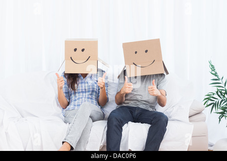 Couple avec des boîtes en carton sur la tête giving Thumbs up Banque D'Images