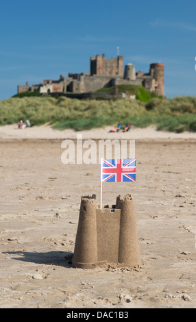 Union Jack flag dans un château de sable sur la plage en face du château de Bamburgh. Northumberland, Angleterre Banque D'Images