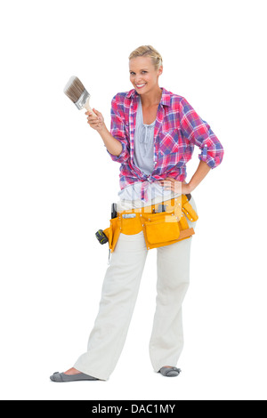 Smiling woman holding paint brush portant une ceinture d'outils Banque D'Images