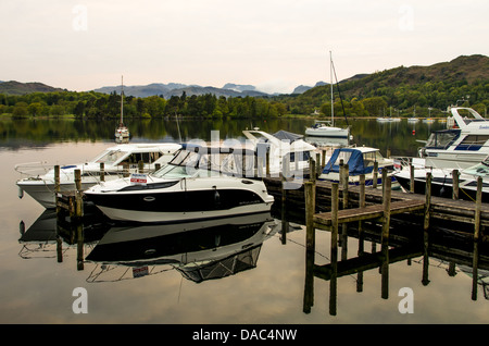 Une jetée en bois sur Windermere avec peu de bateaux de vitesse dans l'avant-plan et de yachts, les arbres et les collines au loin. Banque D'Images