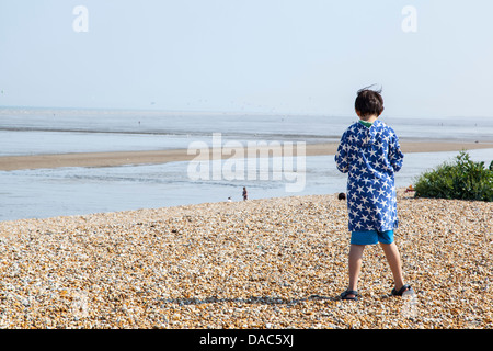 Garçon debout sur la plage, veste bleue avec motif blanc, bord de plage avec un garçon debout, face à la plage Banque D'Images