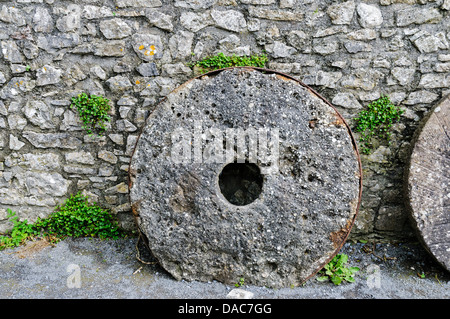 Une vieille meule appuyée contre un mur de pierre médiéval au château de Carew, Pembrokeshire, Pays de Galles Banque D'Images