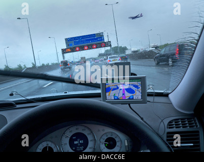 M25 Wet autoroute pluie vue conducteur POV SAT NAV trafic Heathrow conditions humides aéroport, avion en finale limite de vitesse rouge sur le pont roulant Surrey UK Banque D'Images