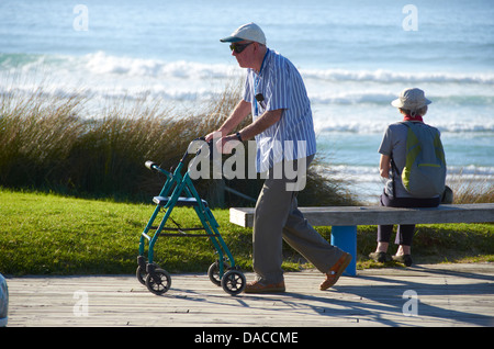 Homme âgé marche sur la promenade avec une dame assis à l'extérieur, vers l'océan Pacifique à l'arrière-plan. Banque D'Images