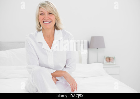 Happy woman sitting cross legged dans sa chambre à coucher Banque D'Images