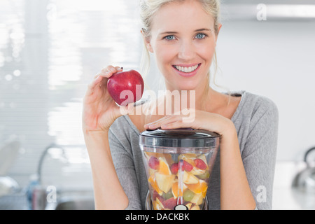 Femme blonde appuyée sur son centrifugeuse plein de fruits et holding Red Apple Banque D'Images