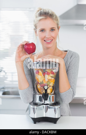 Pretty woman leaning on sa centrifugeuse, plein de fruits et holding Red Apple Banque D'Images