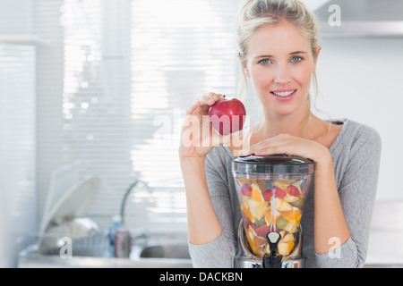 Happy woman leaning on sa centrifugeuse, plein de fruits et holding Red Apple Banque D'Images