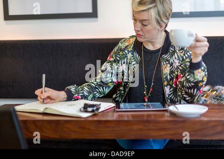 Femme écrit dans le bloc-notes in cafe Banque D'Images