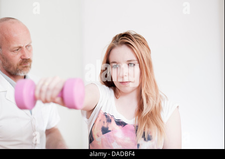 Young woman exercising with dumb bells, guidée par man Banque D'Images