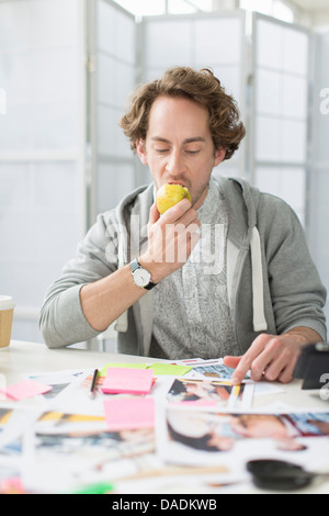 Young man eating apple au bureau en bureau de création Banque D'Images