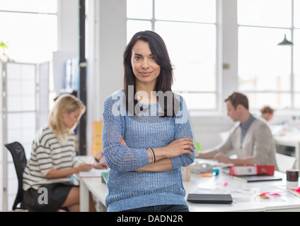 Mid adult woman sitting on desk and smiling in creative office, portrait