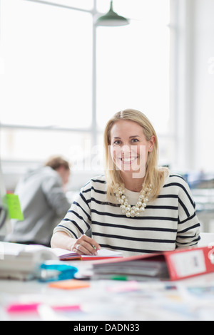 Young woman sitting at desk and smiling in creative office, portrait Banque D'Images