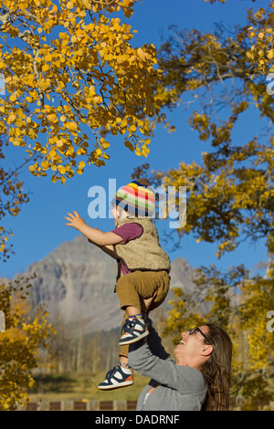 Mother holding up toddler parmi les arbres d'automne Banque D'Images