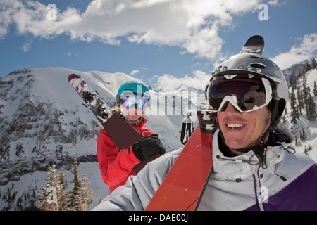 Jeune femme et Mid adult man in skiwear transportant des skis sur l'épaule, smiling Banque D'Images