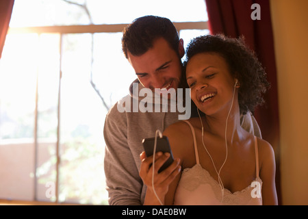 Jeune couple listening to mp3 player in hotel room, smiling Banque D'Images