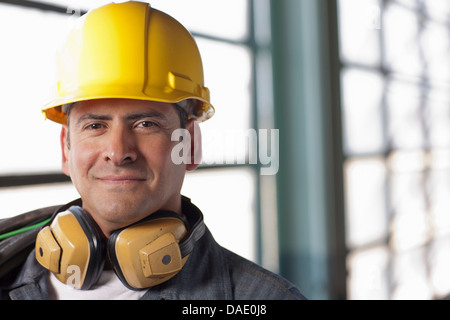 Young construction worker wearing hard hat et oreilles, smiling Banque D'Images