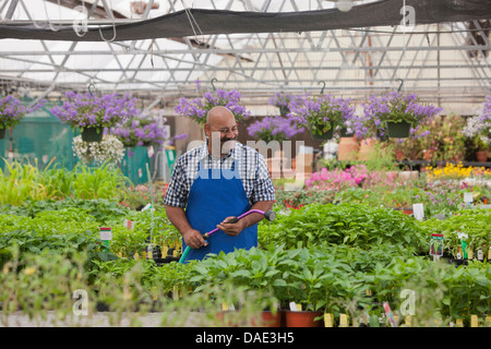 Jardinier l'arrosage des plantes matures en centre-jardin, smiling Banque D'Images