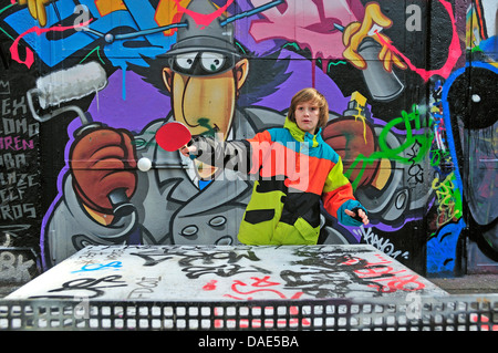 Garçon de douze ans à jouer au tennis de table en face de mur de graffiti, Allemagne, Berlin, Cologne Banque D'Images