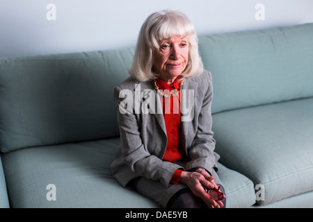 Senior woman sitting on sofa avec expression vide Banque D'Images