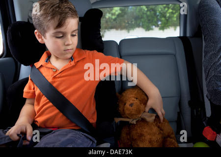 Garçon en siège pour enfant en voiture avec ours Banque D'Images