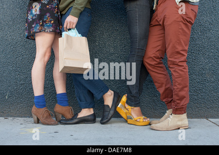 Quatre jeunes adultes debout par wall, low section Banque D'Images