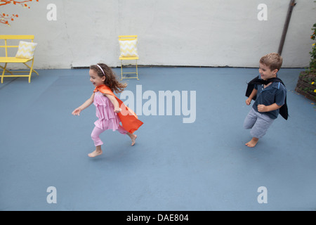 Boy and girl wearing superhero capes jouer en cour arrière Banque D'Images