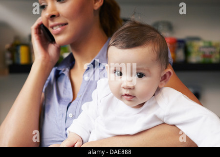 Mother holding baby girl alors que sur le téléphone Banque D'Images