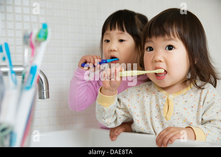 Les tout-petits de deux filles se brosser les dents à l'évier de salle de bains Banque D'Images
