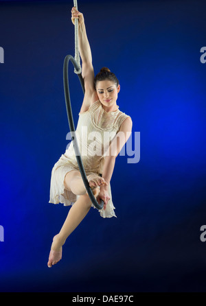 Aerialist poised on hoop against blue background Banque D'Images