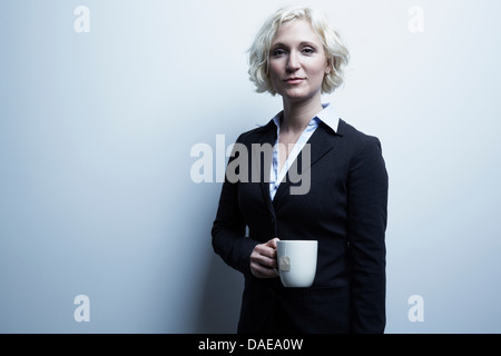 Studio portrait of blond businesswoman holding mug de thé Banque D'Images