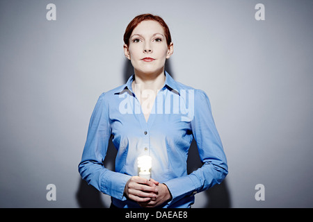 Studio portrait of young woman holding allumé lightbulb Banque D'Images