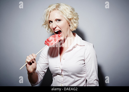 Studio portrait of young woman biting en sucette rouge Banque D'Images