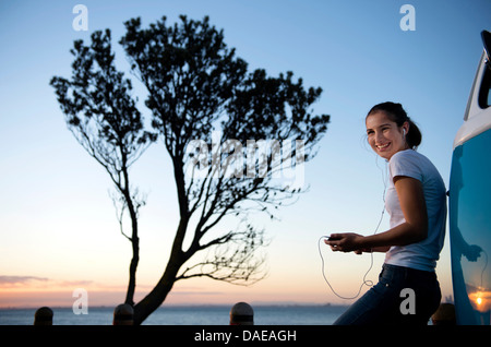 Smiling young woman leaning on camper van au crépuscule Banque D'Images