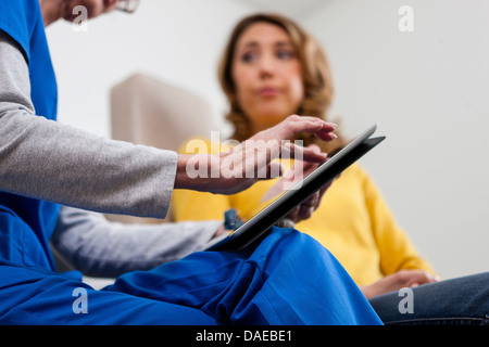 Docteur en bleu frotte using digital tablet with patient Banque D'Images