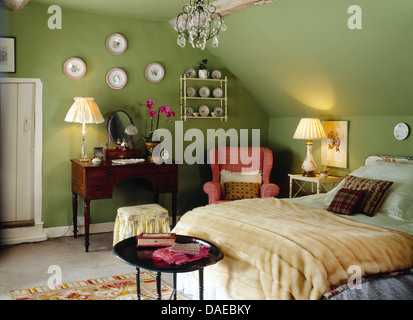 Plaques sur mur au-dessus d''une coiffeuse avec une lampe allumée en vert pays chambre avec fausse fourrure crème jeter sur le lit Banque D'Images