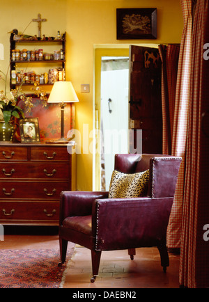 Fauteuil en cuir violet en jaune pays salon avec lampe allumée sur commode ancienne à côté de la porte ouverte Banque D'Images