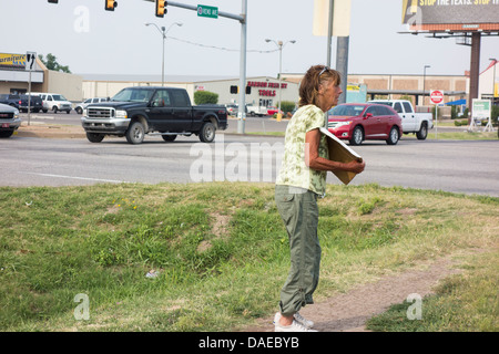 Une vieille femme sans-abri, une pancarte nous amène à une intersection à Oklahoma City, Oklahoma, USA dans une grande zone de trafic. Banque D'Images