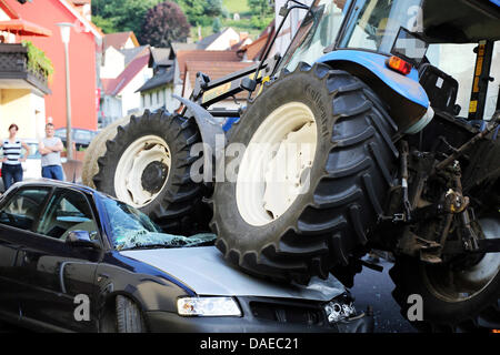 Rothenbuch, Allemagne. 10 juillet, 2013. Un tracteur appartient à deux roues d'une voiture à Rothenbuch, Allemagne, 10 juillet 2013. Les 82 ans de pilote le tracteur qui transportait une balle de foin a mal jugé la distance à une voiture en stationnement et a poursuivi sa route vers elle. Le tracteur n'était pas endommagé, mais la voiture a été atteint. Photo : RALF HETTLER/dpa/Alamy Live News Banque D'Images