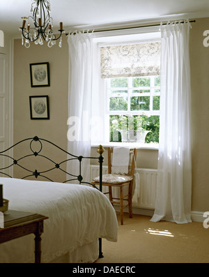 Les draps blancs sur le fer forgé lit dans chambre avec gris pâle voile blanc à motifs et des rideaux sur la fenêtre aveugle Banque D'Images