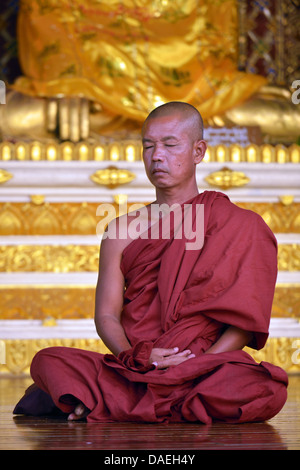 Un moine assis en méditation devant une statue de Bouddha à la pagode Shwedagon, le plus important bâtiment sacré et centre religieux du pays, la Birmanie, Yangon Banque D'Images