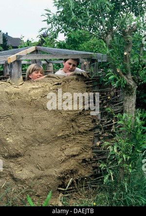 Deux garçons construire une hutte d'argile dans le jardin, Allemagne Banque D'Images