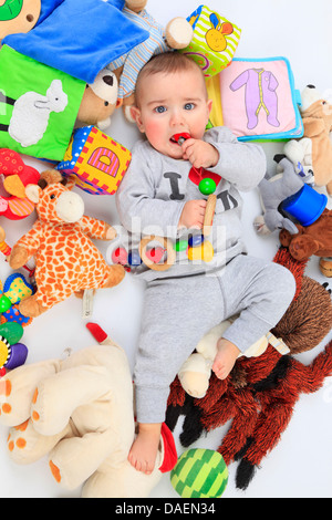 Bébé couché entre jouets en position couchée et suçant un jouet Banque D'Images