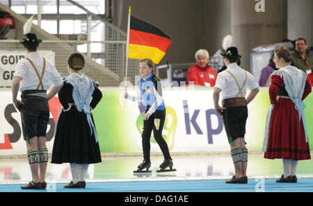 La photo montre un groupe d'hommes et de femmes dansant dans les costumes traditionnels bavarois et une fille de patinage, qui tient le drapeau allemand dans sa main, à la cérémonie d'ouverture du Championnat du Monde Speed-Skating au Aicherner 'Max' Arène à Inzell, Bavière, Allemagne, le 10 mars 2011. Photo : Friso Gentsch Banque D'Images