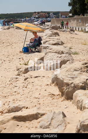 Une femme d'âge moyen sous parapluie de plage de rochers Banque D'Images