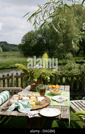 Set de table en bois rustique pour le déjeuner en pays jardin en été avec vue sur le fleuve au-delà de la clôture en bois Banque D'Images