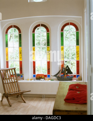 Vitraux fenêtres cintrées sur chant long au-dessus du radiateur, avec chaise en bois et la poitrine en chapelle convertie Banque D'Images