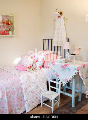 Tissu floral bleu sur table à côté fer à repasser lit avec couette floral et empilé avec coussins à motifs rose dans girl's Bedroom Banque D'Images