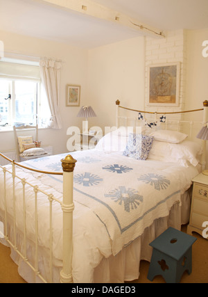 Coussin bleu et blanc +bleu couette sur lit en laiton vintage white cottage chambre avec poutres apparentes peintes en blanc et bleu tabouret en bois Banque D'Images